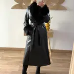 Mujer usando un abrigo largo de polipiel negro con cuello y puños de pelo sintético, combinado con botas negras de tacón.