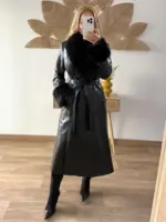 Mujer usando un abrigo largo de polipiel negro con cuello y puños de pelo sintético, combinado con botas negras de tacón.