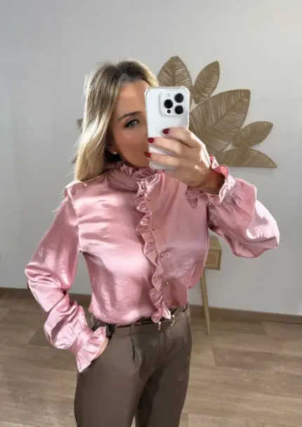 Mujer usando una blusa de satén rosa con volantes frontales y botones dorados, combinada con pantalón marrón de vestir de cintura alta.