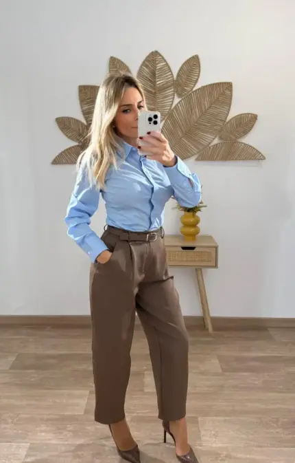 Mujer vestida con camisa azul celeste y pantalón de vestir marrón de cintura alta con cinturón, combinados con tacones marrones.