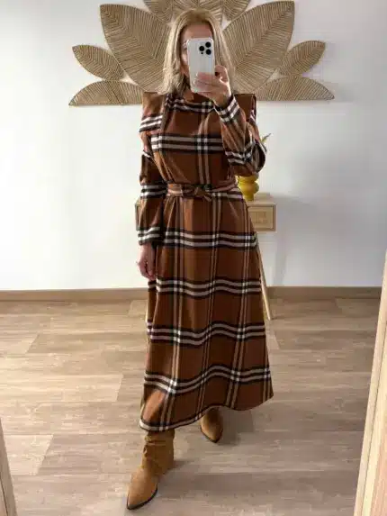 Mujer con vestido largo de cuadros en tonos marrones y beige, de corte recto y cinturón a juego. Lleva botas de ante marrón claro con punta en forma de pico.