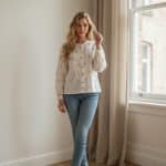 Blusa blanca de manga larga con botones frontales y estampado repetido dorado, cuello redondo fruncido y puños elásticos.