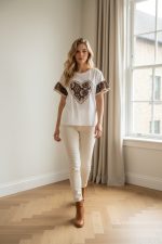 Camiseta blanca de manga corta con parche central en forma de corazón de encaje marrón y mangas con detalle bordado.