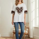 Camiseta blanca de manga corta con parche central en forma de corazón de encaje marrón y mangas con detalle bordado.
