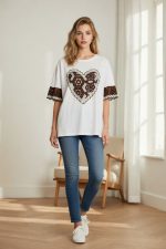 Camiseta blanca de manga corta con parche central en forma de corazón de encaje marrón y mangas con detalle bordado.