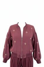 Chaqueta bomber corta color burdeos con cierre de cremallera frontal y bordados pequeños en forma de estrella en toda la prenda.