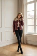 Chaqueta corta de polipiel marrón con cuello de pelo sintético, cierre frontal con botones metálicos y bolsillos con solapa.