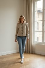 Mujer caminando con chaqueta entallada verde oliva de botones frontales, sin solapas, combinada con pantalón oscuro y zapatillas blancas.