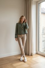 Mujer caminando con chaqueta entallada verde oliva de botones frontales, sin solapas, combinada con pantalón oscuro y zapatillas blancas.