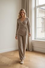 Conjunto femenino de punto en color beige compuesto por top cruzado de manga larga con hebilla lateral y pantalón recto de tiro medio, combinado con zapatillas claras.