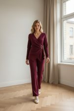 Conjunto femenino de punto en color burdeos compuesto por top cruzado de manga larga con hebilla lateral y pantalón recto de tiro medio, combinado con zapatillas claras.