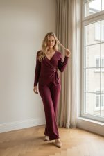 Conjunto femenino de punto en color burdeos compuesto por top cruzado de manga larga con hebilla lateral y pantalón recto de tiro medio, combinado con zapatillas claras.