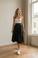 Falda midi azul marino de vuelo con cintura alta y cinturón negro, combinada con blusa beige y botines marrones.