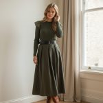 Falda midi verde de vuelo con cintura alta y cinturón negro, combinada con blusa beige y botines marrones.