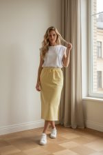 Falda deportiva midi color amarillo pastel con cintura elástica y cordón ajustable, combinada con camiseta blanca y zapatillas.