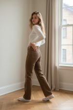 Pantalón vaquero recto de tiro medio-alto en color marrón lavado, con bolsillos delanteros de parche y corte largo, combinado con jersey claro y mocasines marrones.